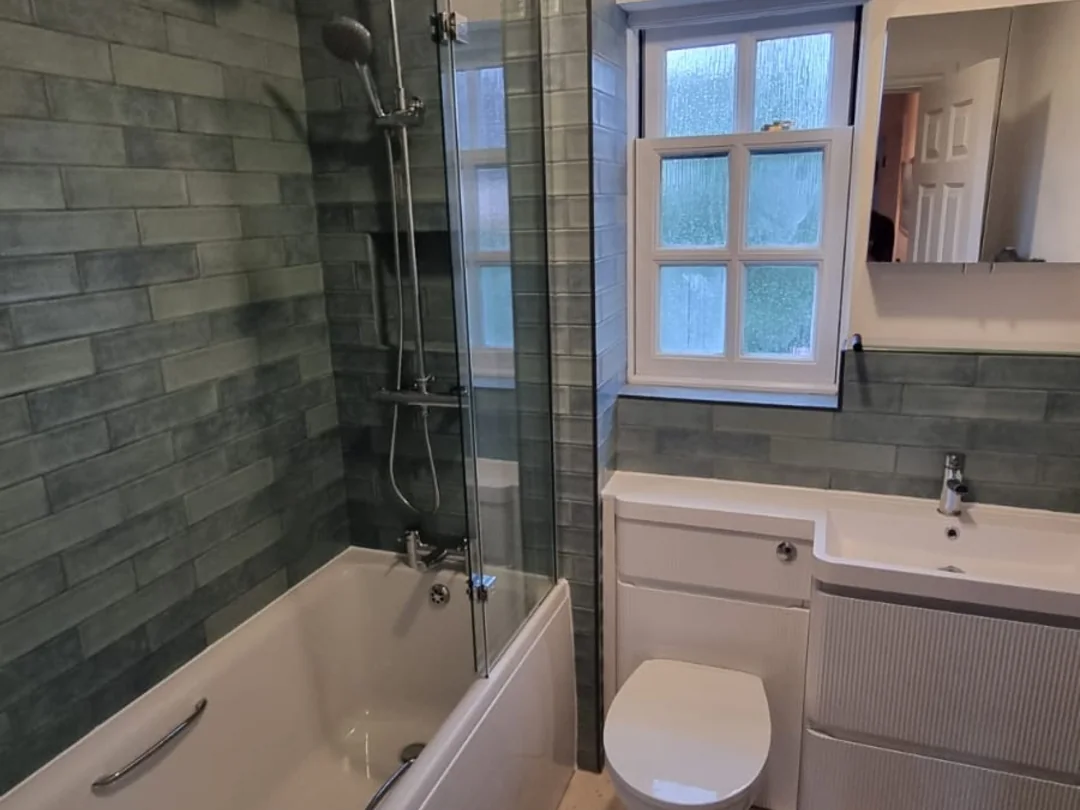 Bathroom fitted by Pete in an older property: bath with a shower over it, green brick-effect tiling, a period window and a fitted vanity unit