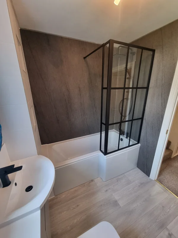 White bath with a black-framed Crittall-style shower screen against dark stone-effect wall panelling