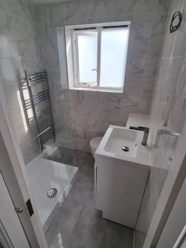 Compact shower room finished in marble-effect tiling with a chrome towel radiator and a fitted basin unit