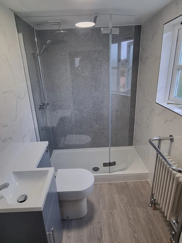 Walk-in shower enclosure with grey stone-effect panelling, marble-effect walls and a traditional column radiator